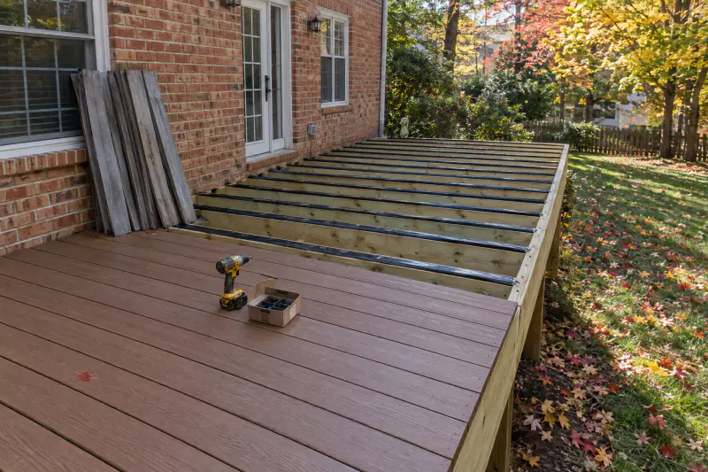 Deck resurfacing in progress with new composite boards and hidden fasteners over taped joists beside stacked old cupped boards