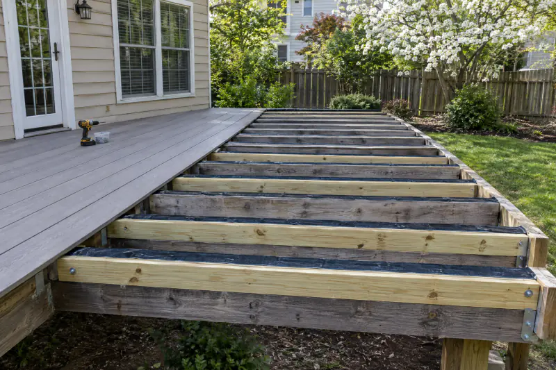 Old deck joists with new sister joists and joist tape, partly covered by new gray composite decking during resurfacing