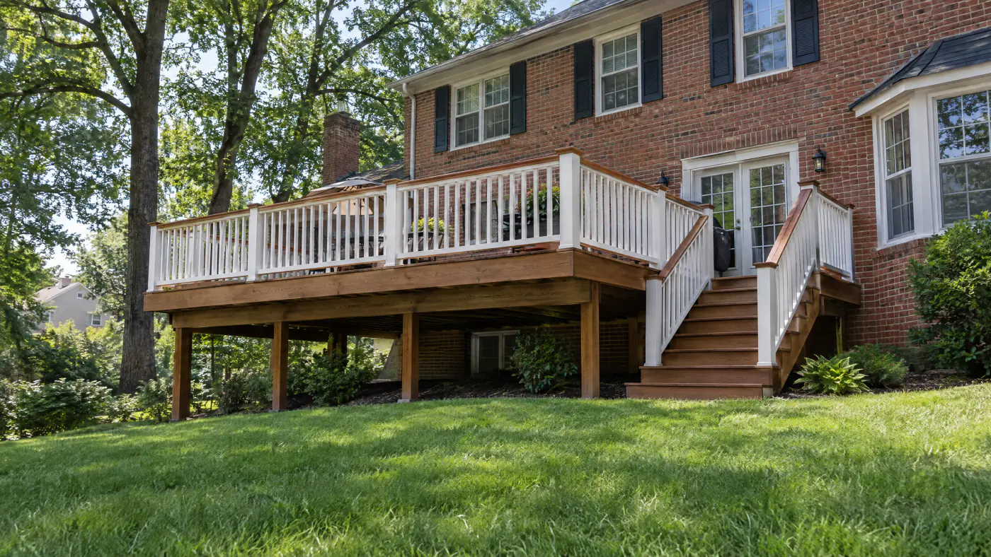 Freshly stained pressure-treated deck in warm brown behind a brick colonial under oak trees on a dry June morning