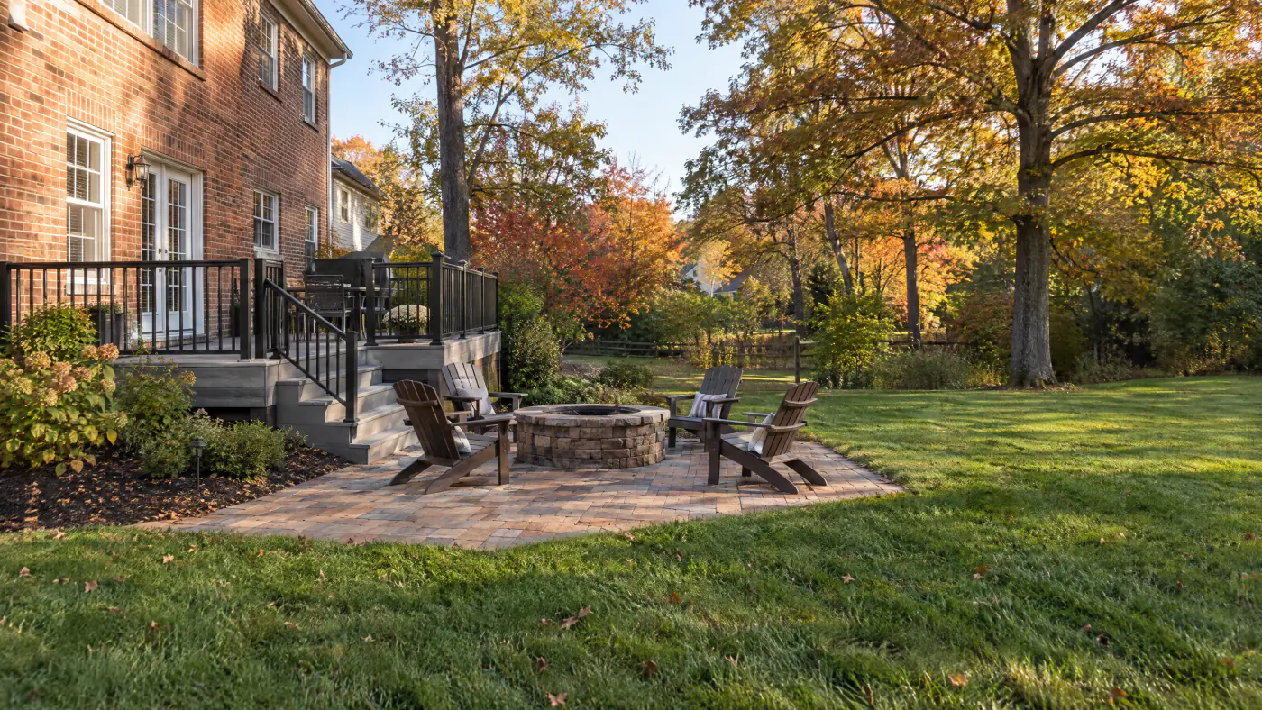 Composite deck stepping down to a paver patio with a fire pit behind a Northern Virginia colonial in fall