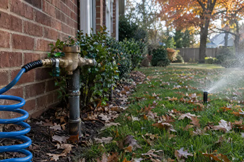 Compressor hose connected to an irrigation backflow preventer beside a brick house during a fall sprinkler blow-out