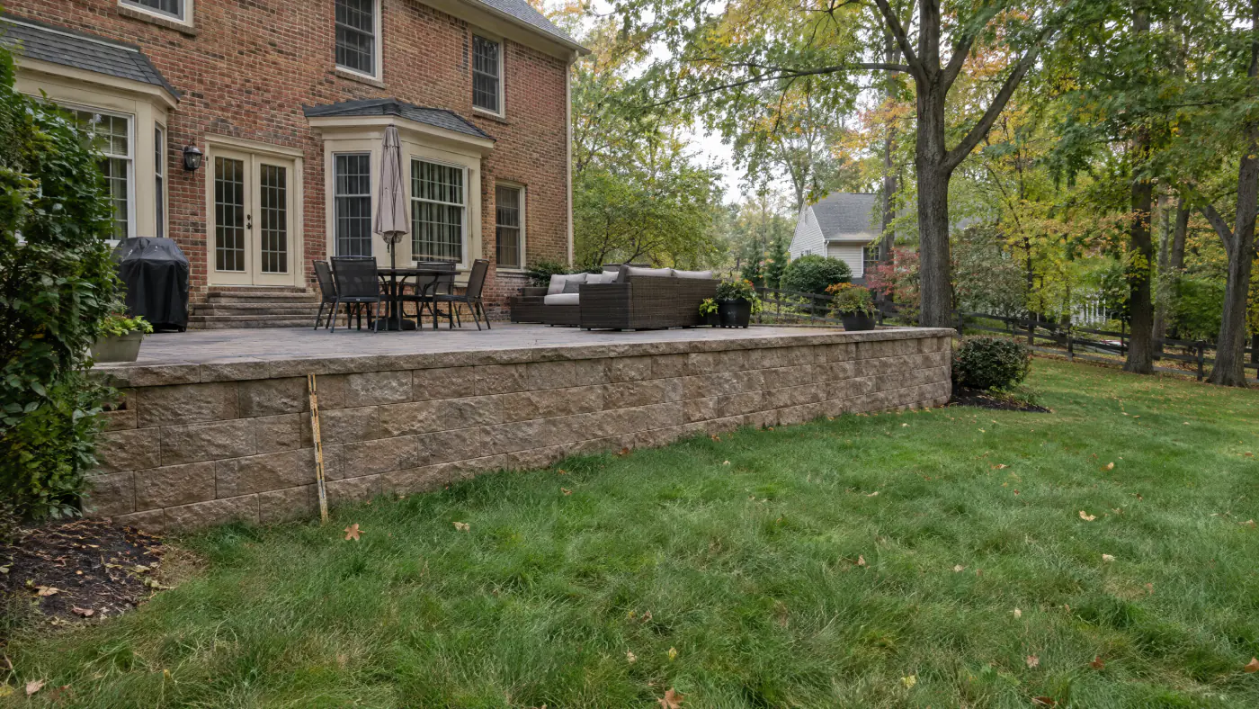 Segmental block retaining wall about three feet tall supporting a paver patio behind a brick colonial in Northern Virginia