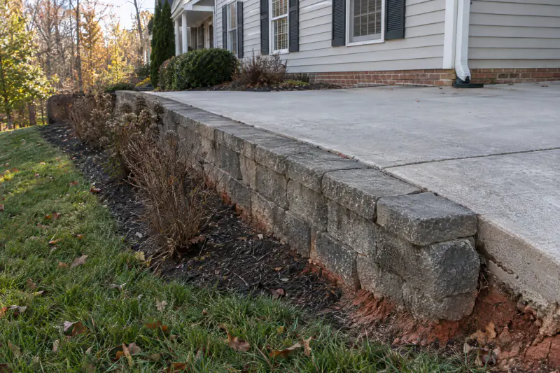 Low block retaining wall holding up the edge of a concrete driveway beside a siding colonial in Northern Virginia