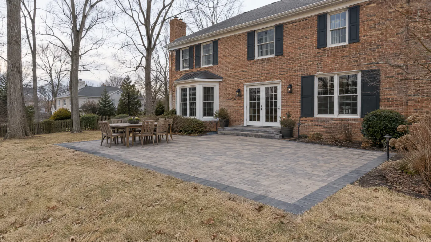 Finished gray paver patio with a dark border behind a brick colonial home in a Northern Virginia backyard