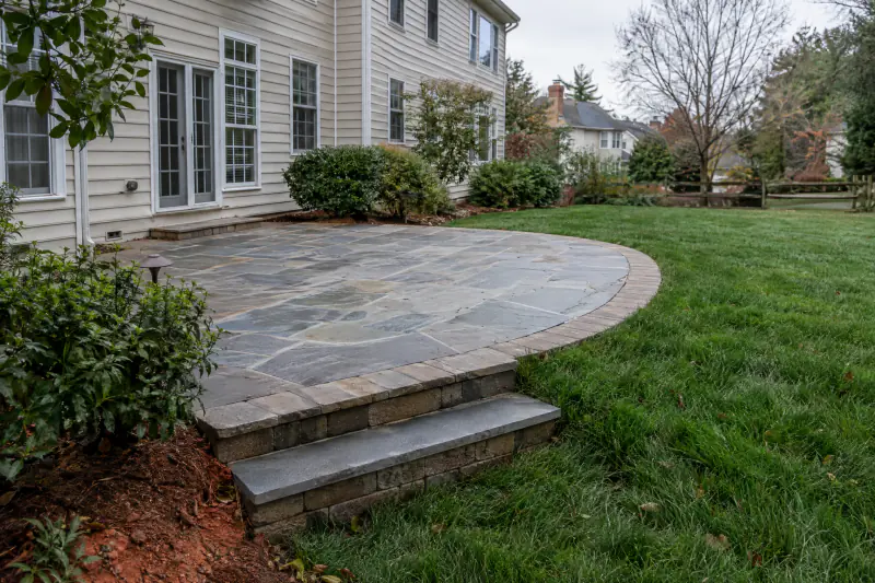 Curved bluestone patio edge with inlaid border and two steps beside a tall fescue lawn in Northern Virginia