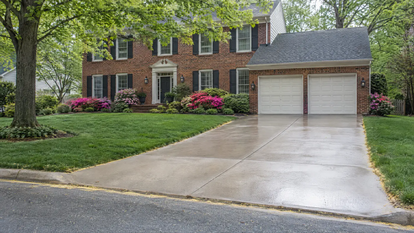 Freshly pressure washed concrete driveway beside a lawn still dusted with yellow pine pollen at a brick colonial