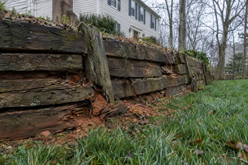 Old timber retaining wall leaning forward with rotted ties and soil spilling onto a lawn in a Northern Virginia yard