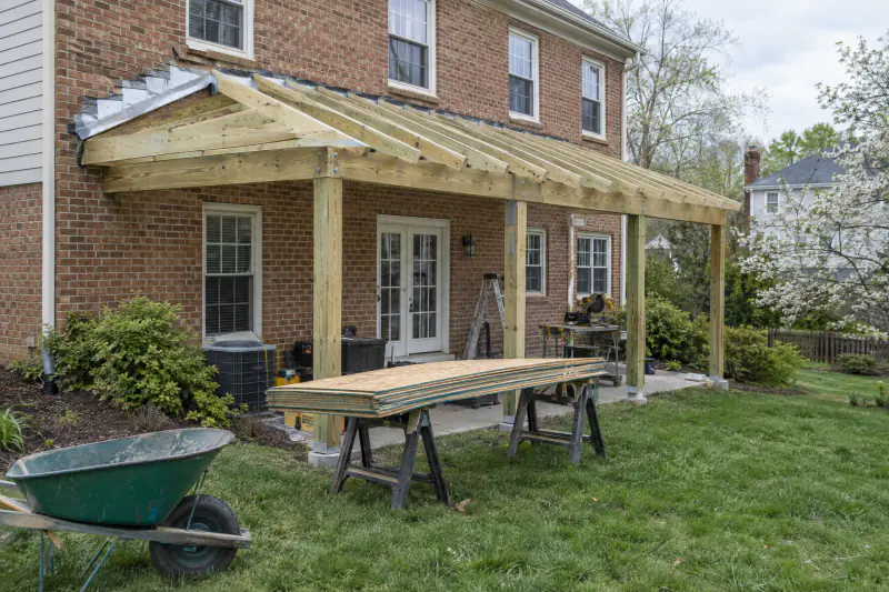Porch roof rafters tied into a house wall with step flashing and a ledger during screened porch framing in Northern Virginia