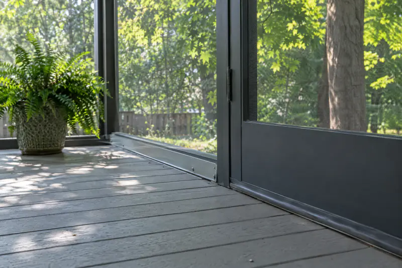 Tongue-and-groove porch flooring meeting an aluminum screen base channel and door sweep on a Northern Virginia screened porch