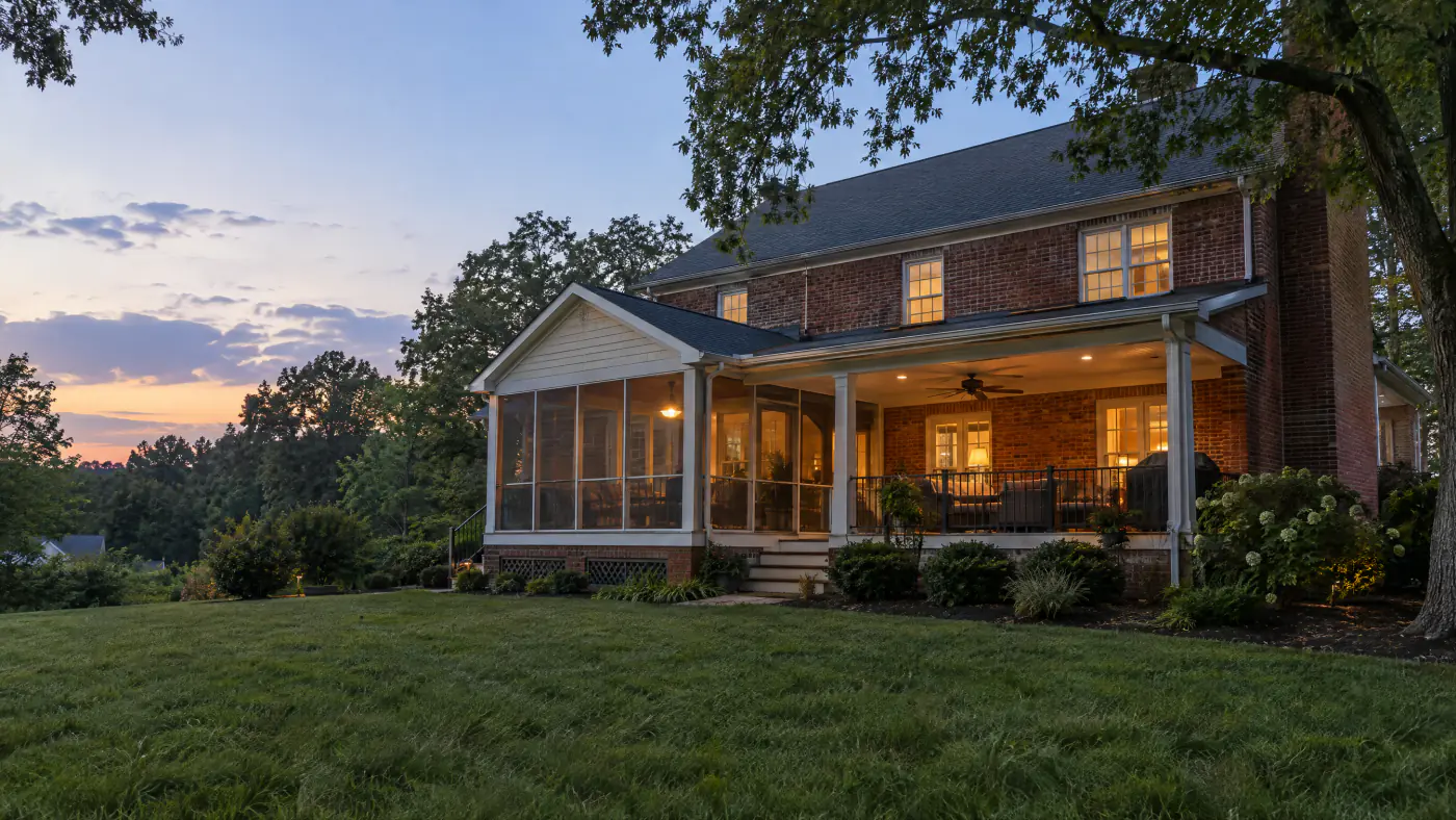 Screened porch beside an open covered porch on the back of a brick colonial home in a Northern Virginia backyard at dusk