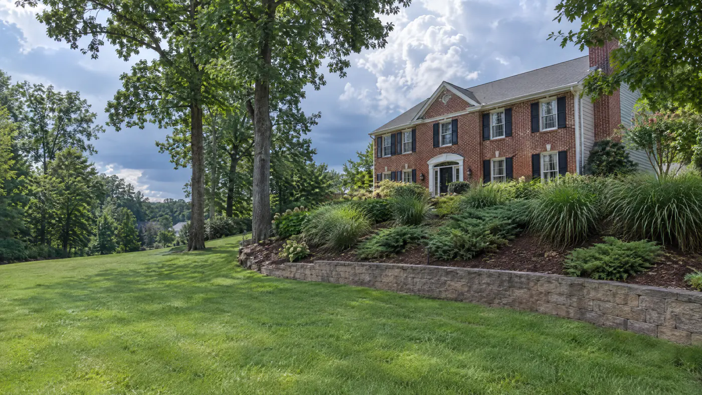Terraced backyard slope in Northern Virginia with a low block wall, planted bank and brick colonial above