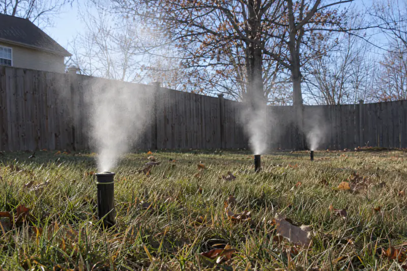 Pop-up rotor sprinkler heads blowing mist across a dormant lawn during a compressed air winterization