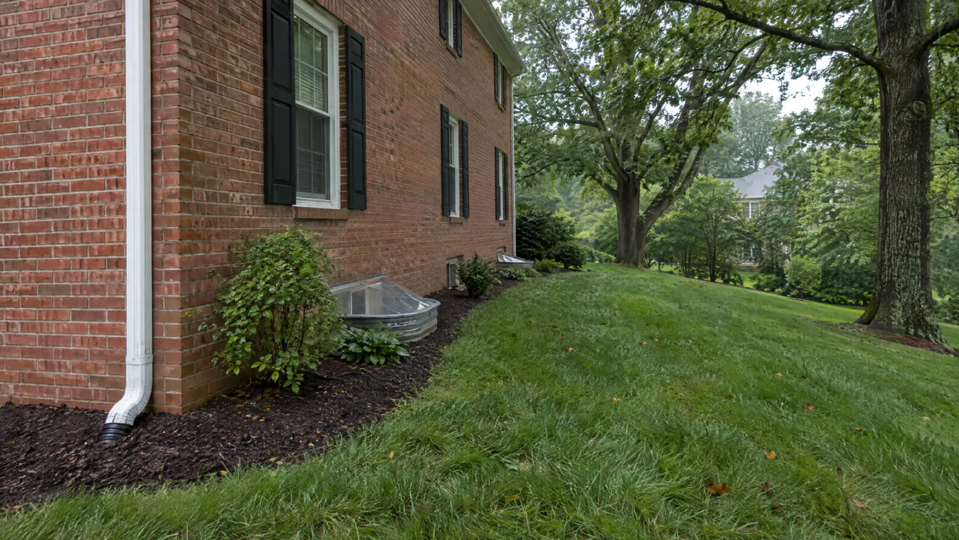 Downspout extension carrying roof water across a lawn away from a brick colonial foundation in Northern Virginia