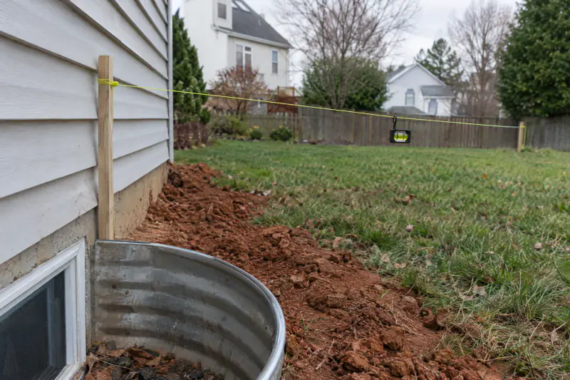 String line and level showing the ground sloping away from a house foundation beside a basement window well