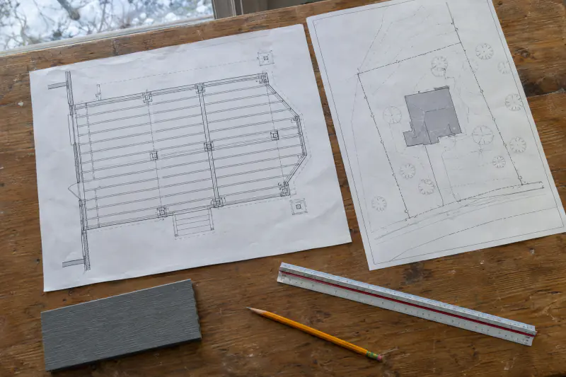 Deck framing plan and plat laid out on a workbench with a scale ruler and composite decking sample