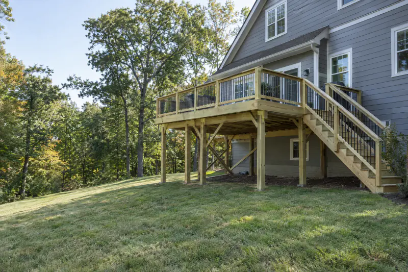 New elevated pressure-treated custom deck with stairs behind a craftsman home