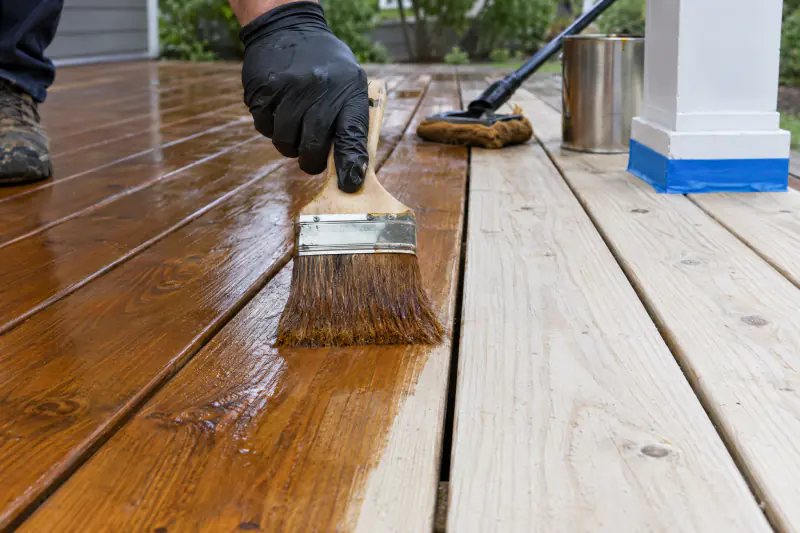 Brush applying semi-transparent stain to clean boards during deck cleaning and staining