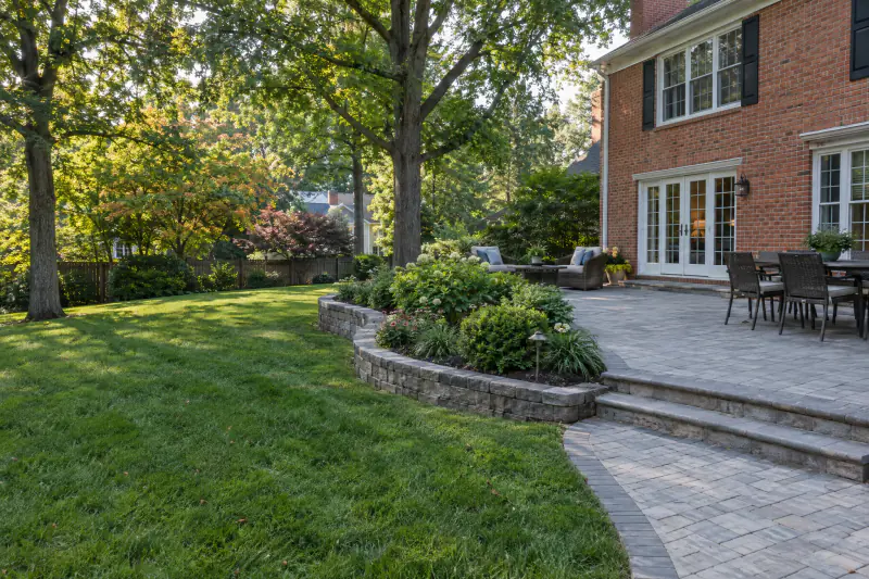 Finished hardscaping with paver patio, walkway and low retaining wall behind a brick home