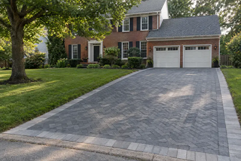 Herringbone paver driveway with border leading to brick colonial two-car garage