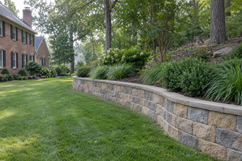 Curved segmental block retaining wall holding a planted slope behind a brick home