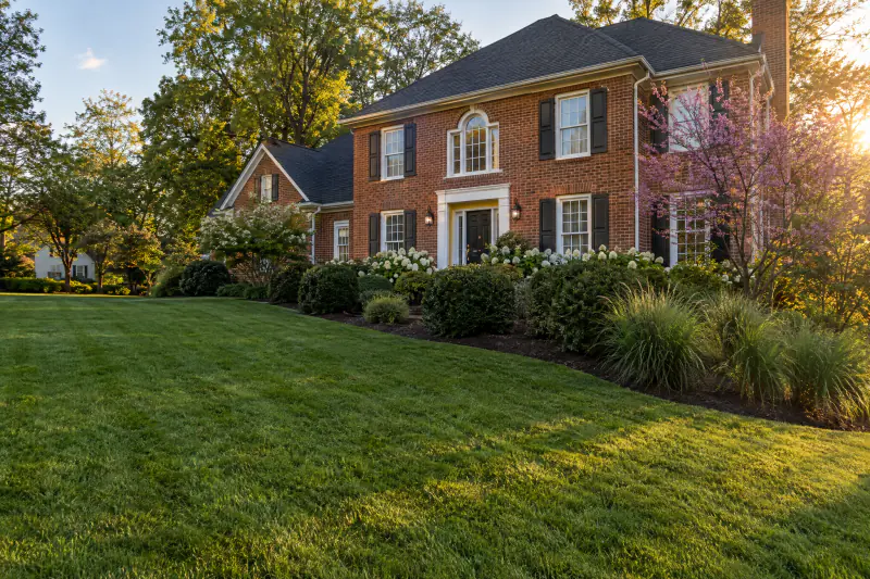 Lush fescue lawn and layered landscape beds in front of a brick colonial home